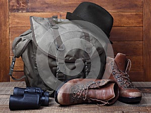 Rucksack with old boots, binoculars and hat on wooden background
