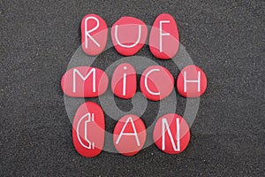 Ruf mich an, call me, german text composed with red painted stone letters over black sand