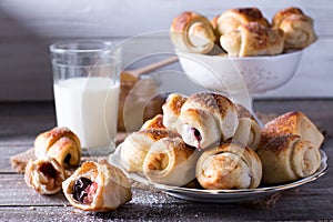 Rugelach with jam filling on plate with milk on wooden background