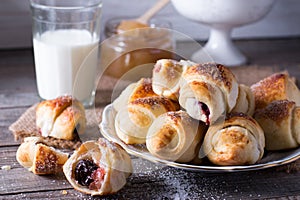 Rugelach with jam filling on plate with milk on wooden background