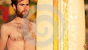 Rugged bearded male surfer portrait next to surf board