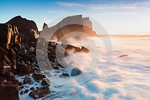 Rugged Icelandic coastline with big waves hitting the black rocks in south west Iceland. Typical Icelandic landscape sunrise