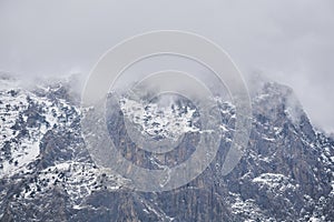 Rugged mountain landscape - snow-capped rocky cliffs with rare trees hide in cloudy fog