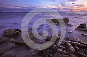 A rugged and rocky seascape at sunrise with waves flowing over harsh granite rocks.