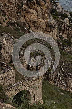 Ruin of medieval stone fort on rocks with arch in highlands of Dagestan in summer, detail of abandoned and destruction building.