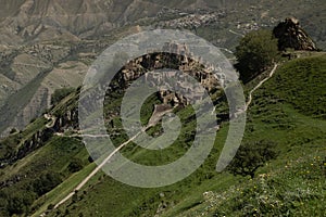 Ruin of old stone castle on peak of in mountain in Dagestan with destruction houses, majestic mountain landscape with green slopes