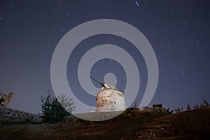 Ruin windmill in the night sky. A view of the stars of the Milky Way with a mountain top in the foreground.