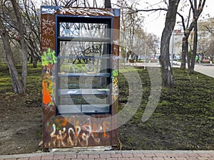 Ruined, broken, and scribbled public bookcase outdoors in the park. Vandalism concept. Street library