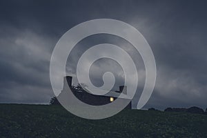 A ruined house in the middle of the countryside. With a light shining from a broken window on a stormy night