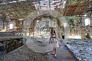 Ruined old abandoned factory and a young girl inside looks at the ruins.
