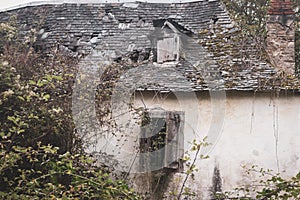 Ruined old house in abandoned garden. Ancient rural architecture in France. Destroyed building with plants on the roof.