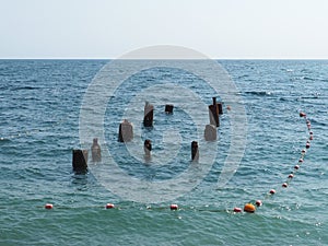 Ruined pier against the backdrop of the deep sea. Wooden poles stick out of the blue water. Black Sea in sunny weather
