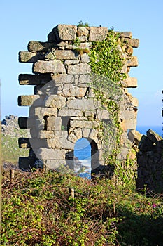 A ruined wall of Treen Cove tin mine with arch stands on the cliff top with Gurnard\'s Head Head behind, Cornwall, England