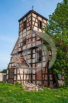 Ruins of the abandoned evangelical church made as half-timbered house with wood and red bricks. Blue sky and green grass and tree