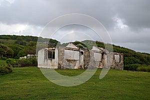 Ruins of an ancient stone building in a bright green field surrounded by trees under a cloudy sky