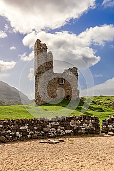 The ruins of Ardvreck Castle, set in the Scottish Highlands, rise above a stone wall, framed by a picturesque sky