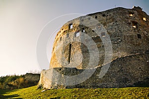 Ruins of castle at sunset with sunrays on the top. Illuminated Castle on the green meadow with blue sky