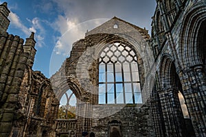 The ruins of Holyrood Abbey still stand tall silhouetted by blue sky and fluffy clouds behind the Queen`s Gallery Palace