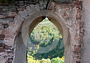 Zrúcanina starého hradu na kopci objatá jesenným lesom.