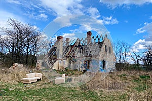 The ruins of an old destroyed house in a field against the blue sky