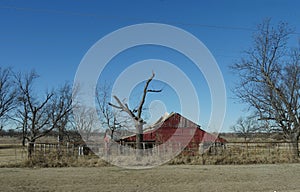 Ruins of a red barn on a farm land along the road