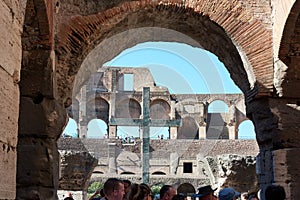 Ruins and stone cross inside the Roman Colosseum, tourists visiting ancient ruins from famous gladiators arena