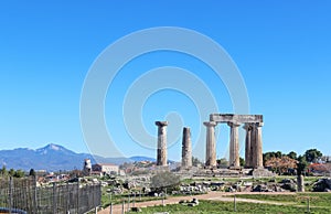 The ruins of the Temple of Apollo at ancient Corith Greece with a church and village and high mountains in the background