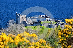 Ruins of Urquhart Castle against boat on Loch Ness in Scotland photo