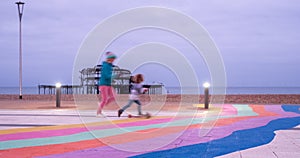 The ruins of West Pier, Brighton, East Sussex, UK. In the foreground, children playing and pavement painted in rainbow stripes.