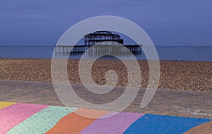 The ruins of West Pier, Brighton, East Sussex, UK. In the foreground, pebble beach and pavement painted in rainbow stripes.