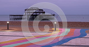 The ruins of West Pier, Brighton, East Sussex, UK. In the foreground, pebble beach and pavement painted in rainbow stripes.