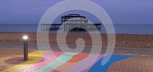 The ruins of West Pier, Brighton, East Sussex, UK. In the foreground, pebble beach and pavement painted in rainbow stripes.