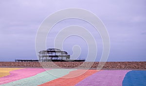 The ruins of West Pier, Brighton, East Sussex, UK. In the foreground, pebble beach and pavement painted in rainbow stripes.