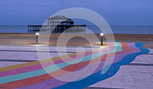 The ruins of West Pier, Brighton, East Sussex, UK. In the foreground, pebble beach and pavement painted in rainbow stripes.