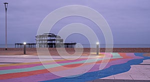The ruins of West Pier, Brighton, East Sussex, UK. In the foreground, pebble beach and pavement painted in rainbow stripes.