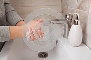 Rules of hand washing. A woman washes her hands between her fingers with liquid soap under a tap of water in the