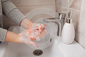 Rules of hand washing. A woman washes her hands between her fingers with liquid soap under a tap of water in the