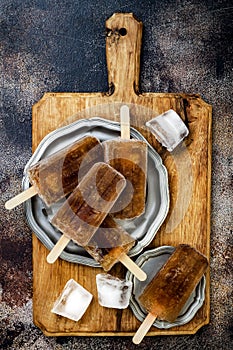 Rum and coke cocktail popsicles with lime juice. Cuba libre homemade frozen alcoholic paletas - ice pops. Overhead, flat lay photo