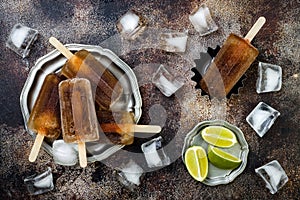 Rum and coke cocktail popsicles with lime juice. Cuba libre homemade frozen alcoholic paletas - ice pops. Overhead, flat lay photo