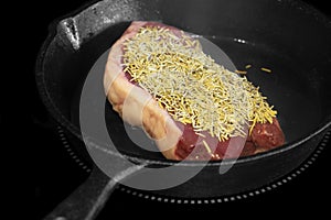 Rump beef steak covered in rosemary cooking on an electric hob stove.