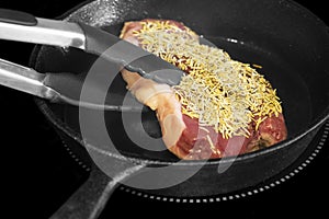 Rump beef steak covered in rosemary,  cooking on an electric hob stove.