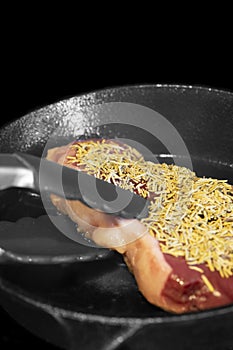 Rump beef steak covered in rosemary,  cooking on an electric hob stove.