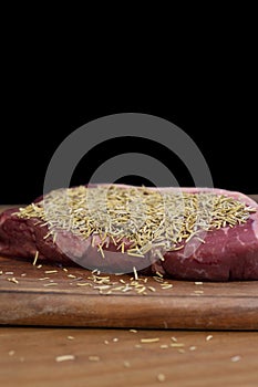 Rump beef steak covered in rosemary on a wooden chopping board.