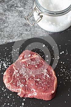 Rump beef steak, seasoned with sea salt with jar in background, on a slate chopping board.