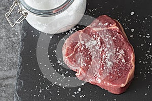 Rump beef steak, seasoned with sea salt with jar in background, on a slate chopping board.