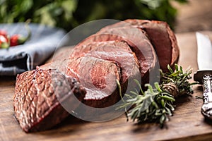 Rump steak cut to slices on a chopping board next to a knife and rosemary