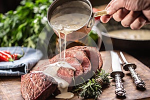 Rump steak cut to slices on a chopping board next to a knife and rosemary, with a mushroom sauce poured over it