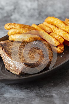 Rump steak dinner, with sweet potato fries and onion rings, on a black oval plate.