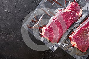 Rump steak in vacuum sealed bag on black textured background, side view space for price