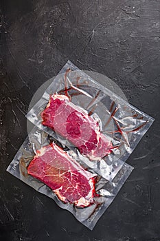 Rump steak in vacuum sealed bag on black textured background, side view space for price